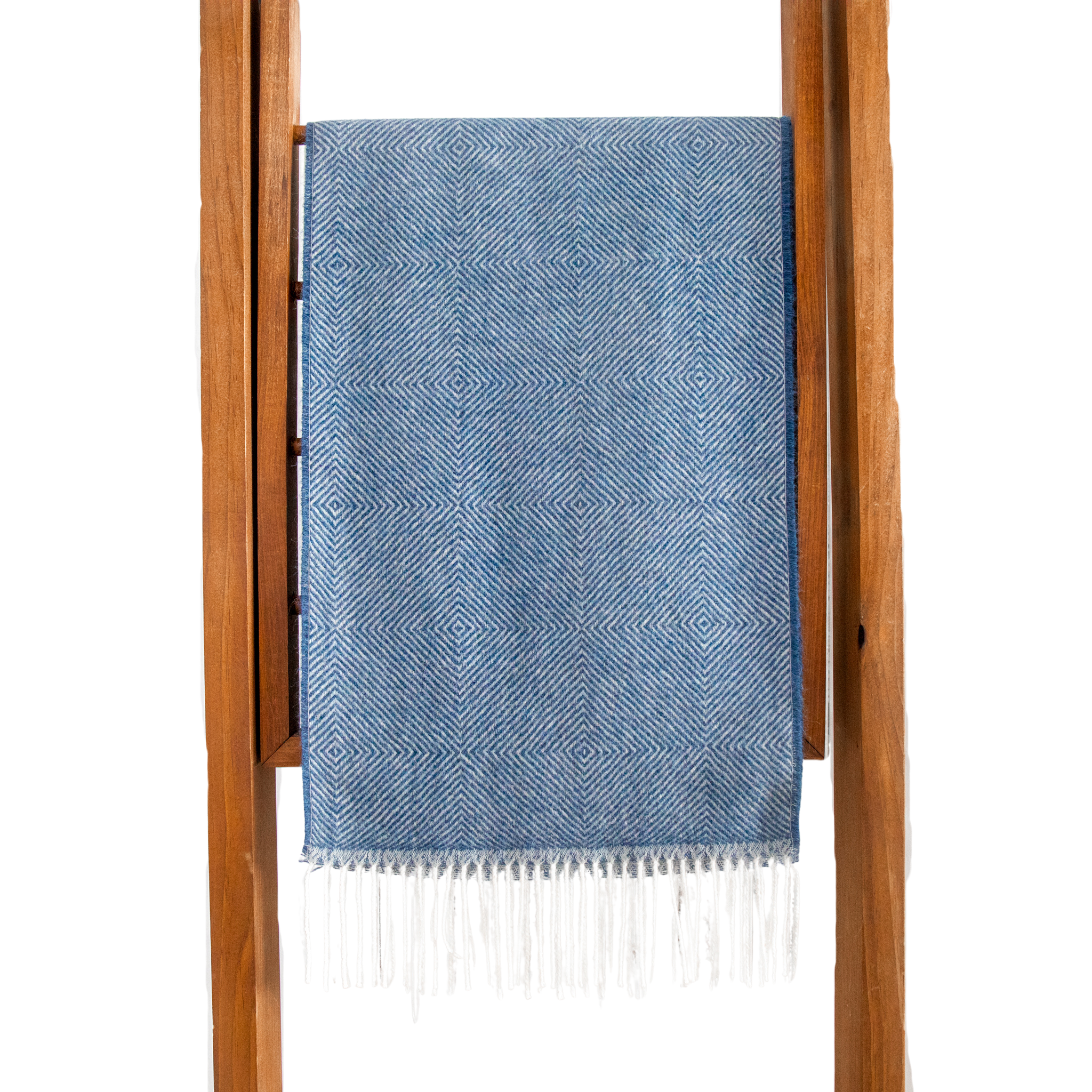 Blue patterned towel with white fringe draped over a wooden rack on a white background