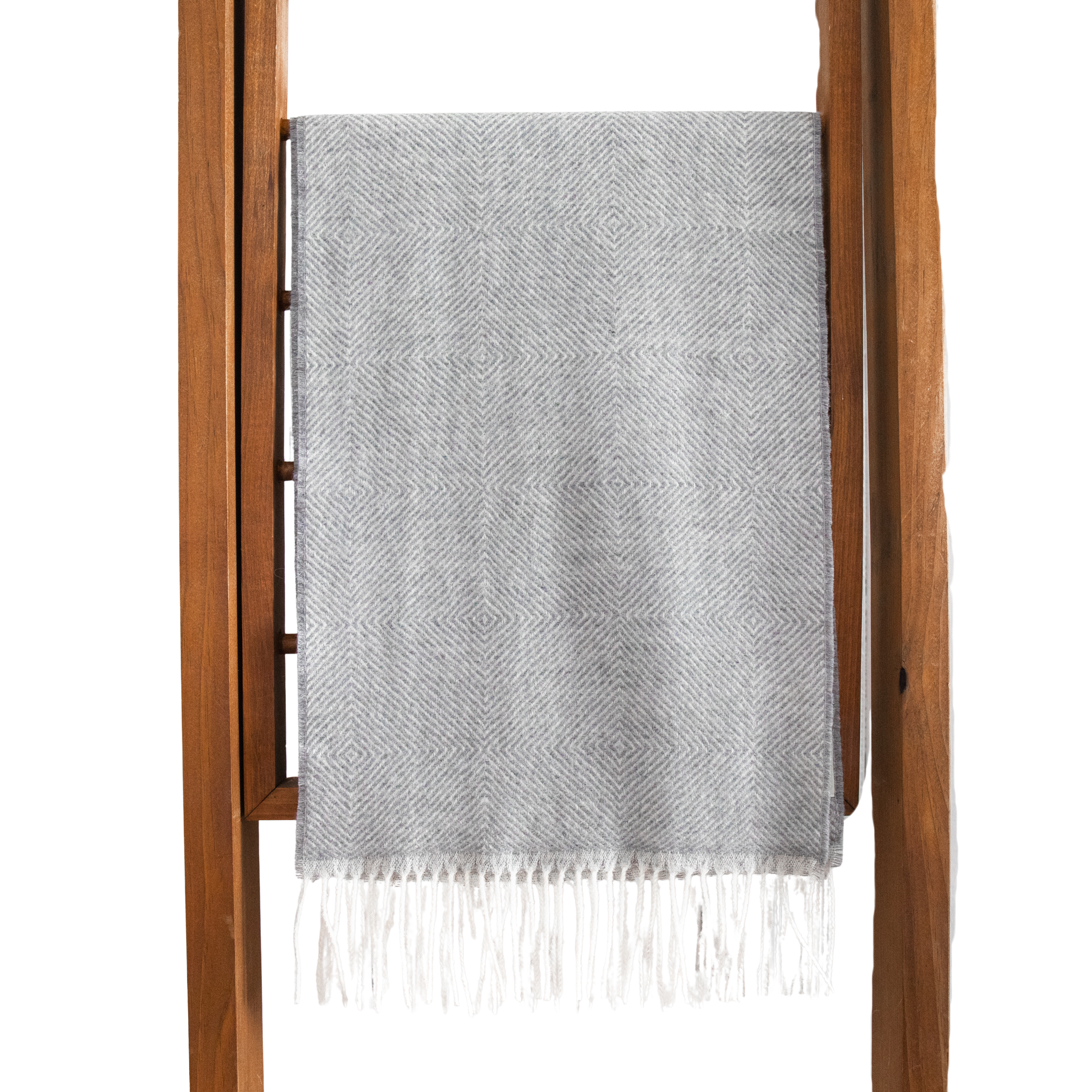 Gray woven blanket with white fringe draped over a wooden ladder on a white background
