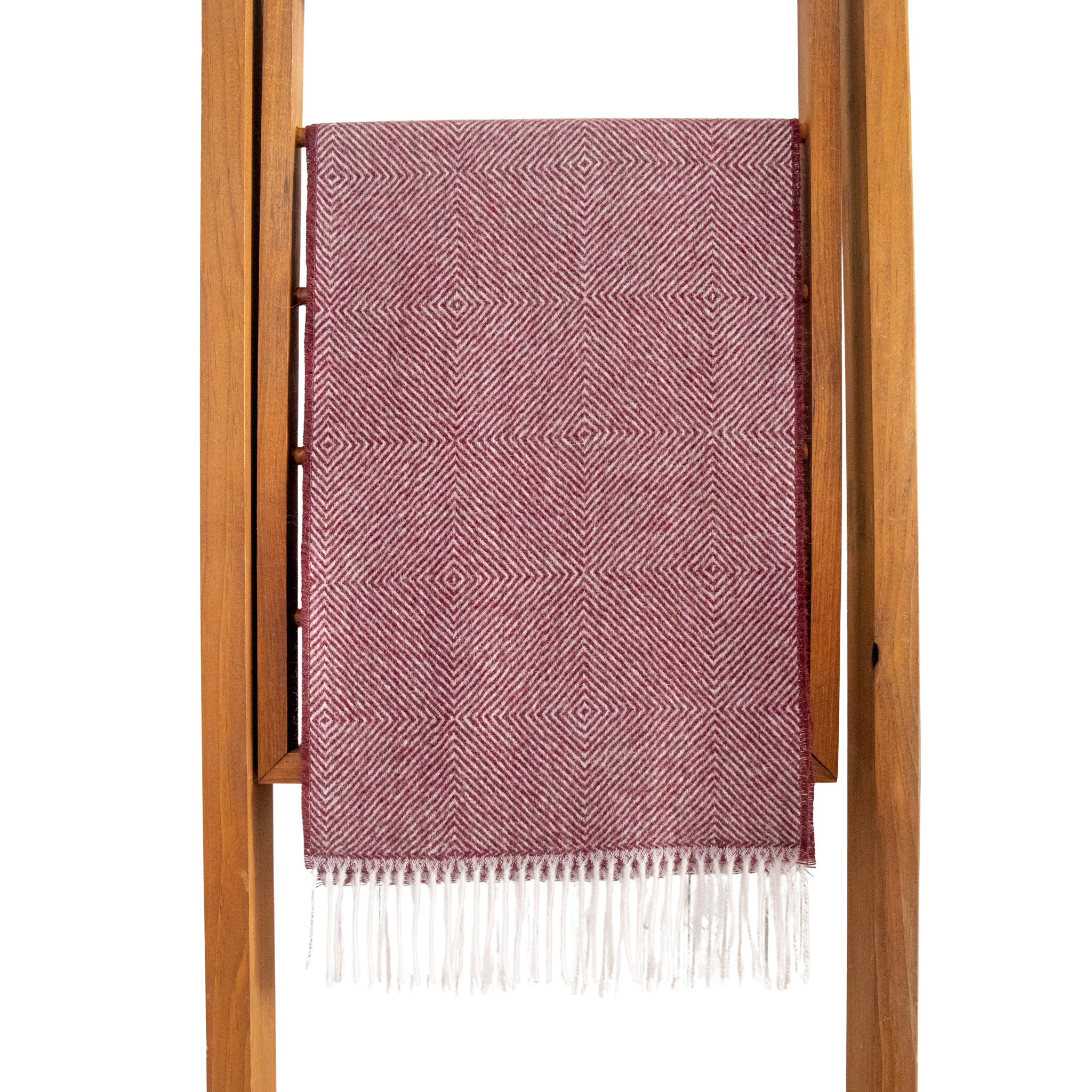 Pink woven blanket with white fringe draped over a wooden ladder on a white background