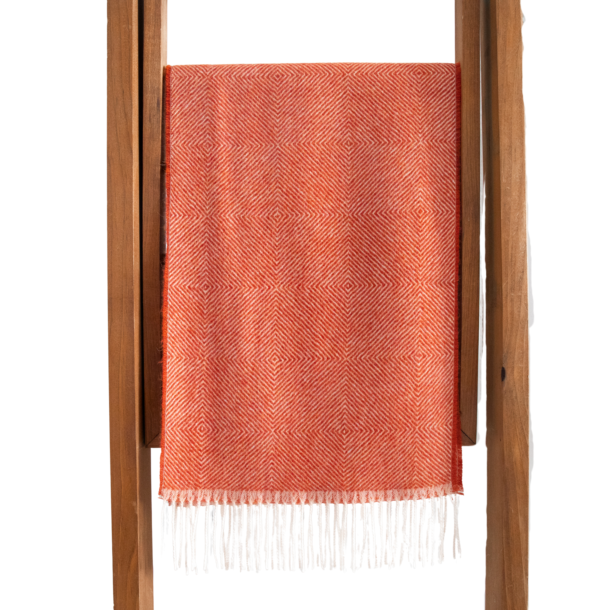 Coral woven blanket with white fringe on a wooden ladder against a white background