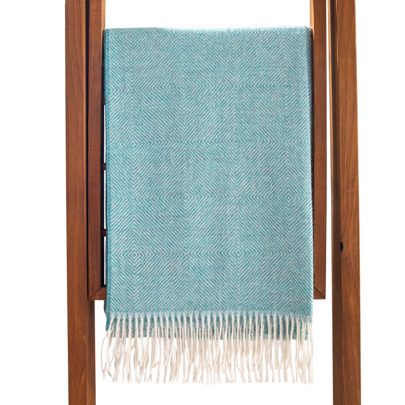 Teal blanket with white fringe draped over a wooden ladder on a white background