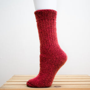 Andinista Alpaca Hiking Socks, a picture of a foot wearing a pair of red alpaca hiking socks on a wooden crate.