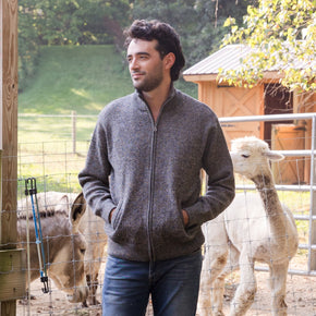 Men's Heavyweight Full-Zip Baby Alpaca Wool Jacket – A man wearing a marled black and white knitted baby alpaca wool zip jacket stands in front of an animal enclosure.