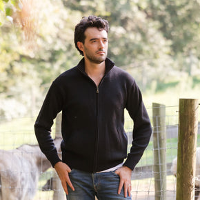 Men's Heavyweight Full-Zip Baby Alpaca Wool Jacket – A man wearing a black knitted baby alpaca wool zip jacket stands in front of an animal enclosure.