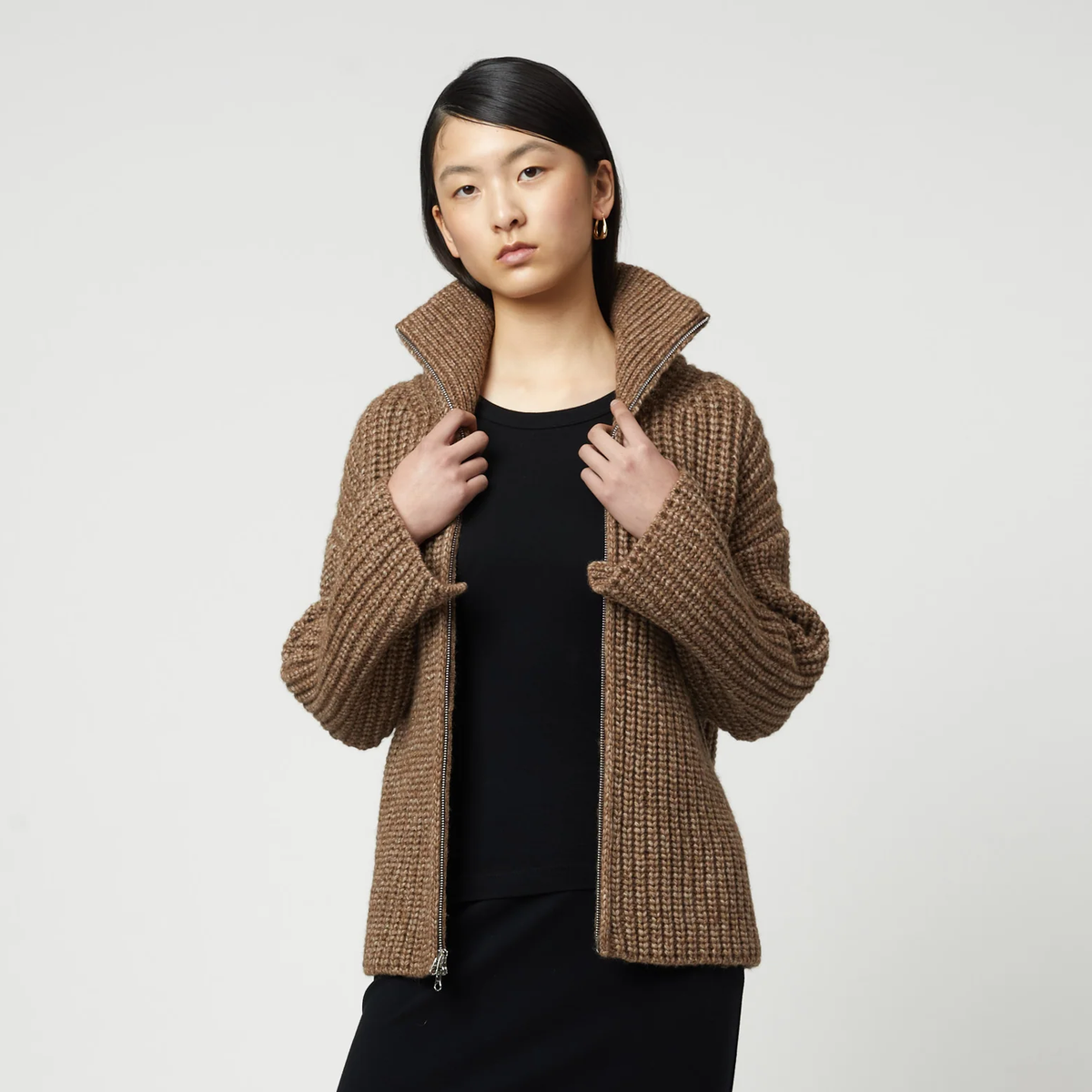 Woman wearing a brown ribbed knit zip-up turtleneck cardigan over a black outfit.