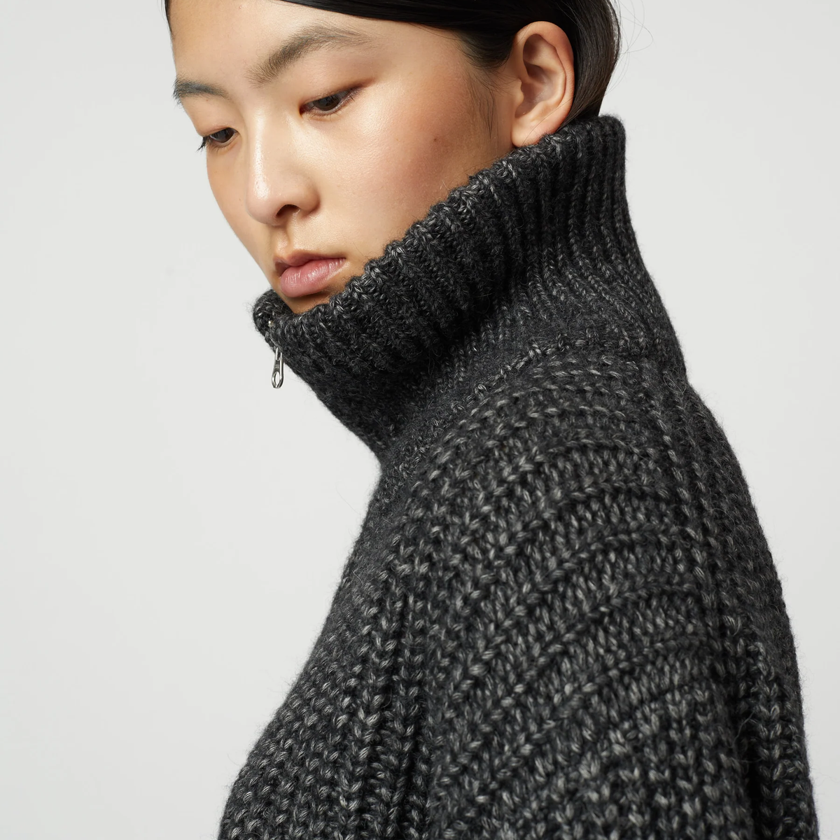 Close up of a woman wearing a charcoal grey ribbed knit zip-up turtleneck cardigan.