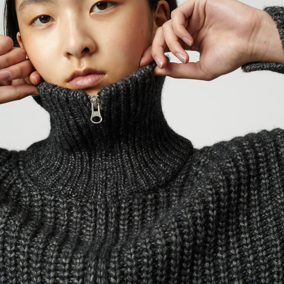 Close up of a woman wearing a charcoal grey ribbed knit zip-up turtleneck cardigan.