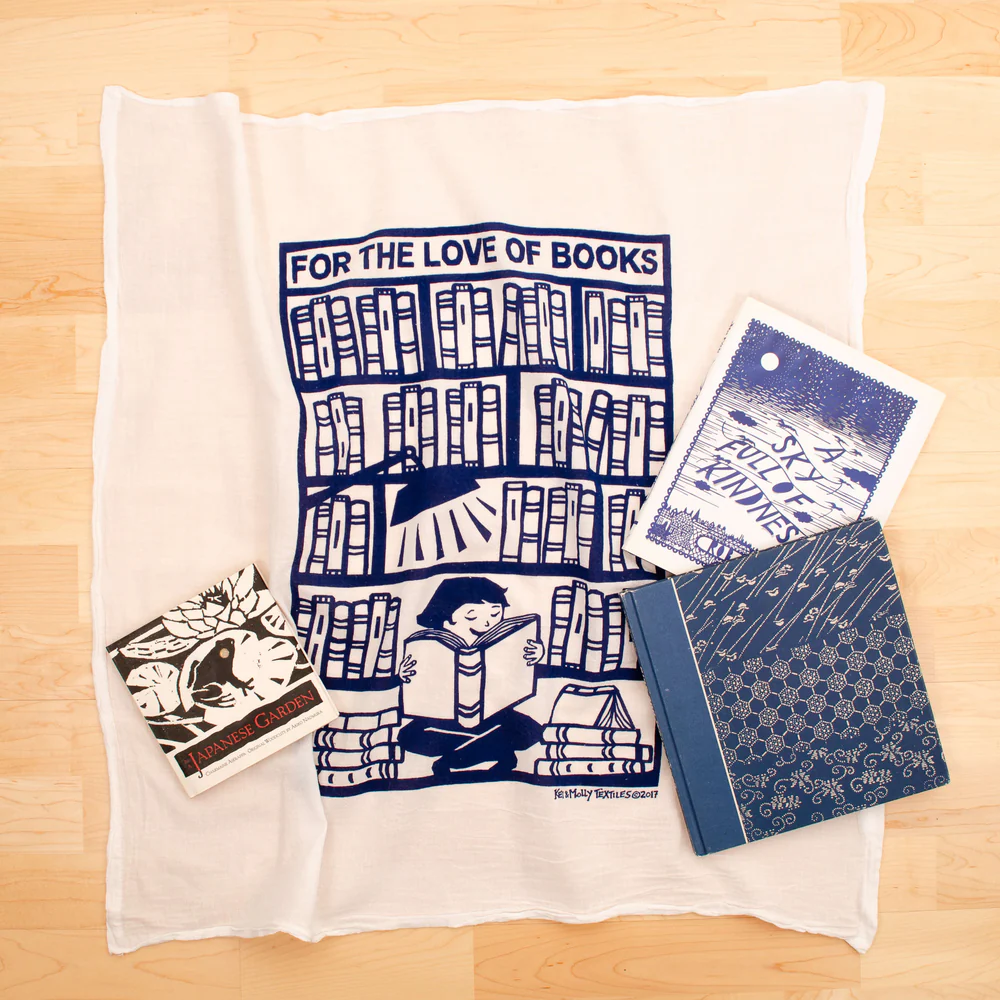 Collection of books and stationery items on a white towel with 'For the Love of Books' design.