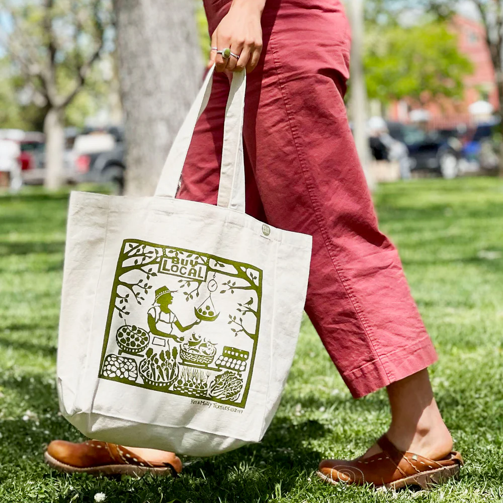 Person holding a white tote bag with green design in a park