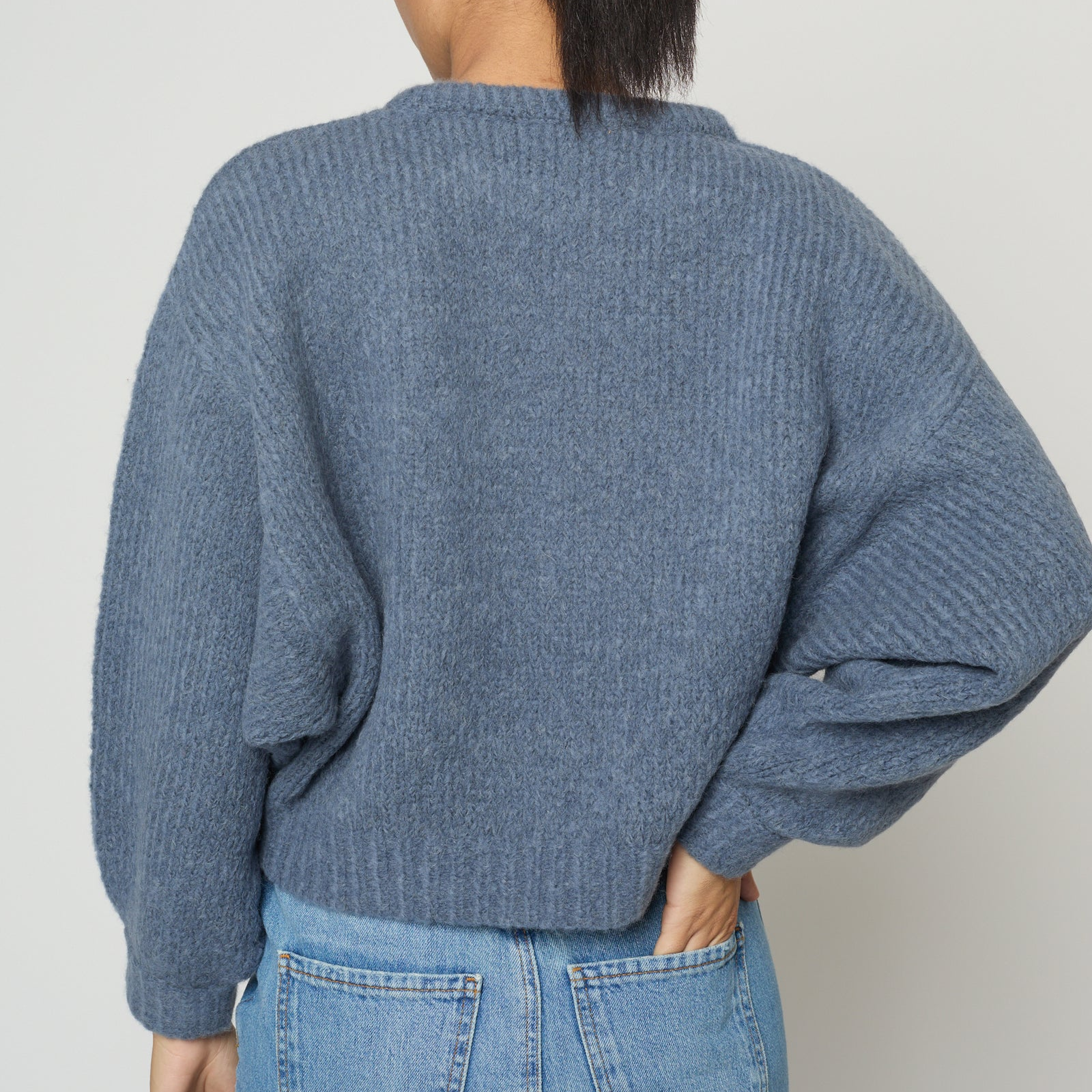 Person wearing a blue knitted sweater and jeans against a white background