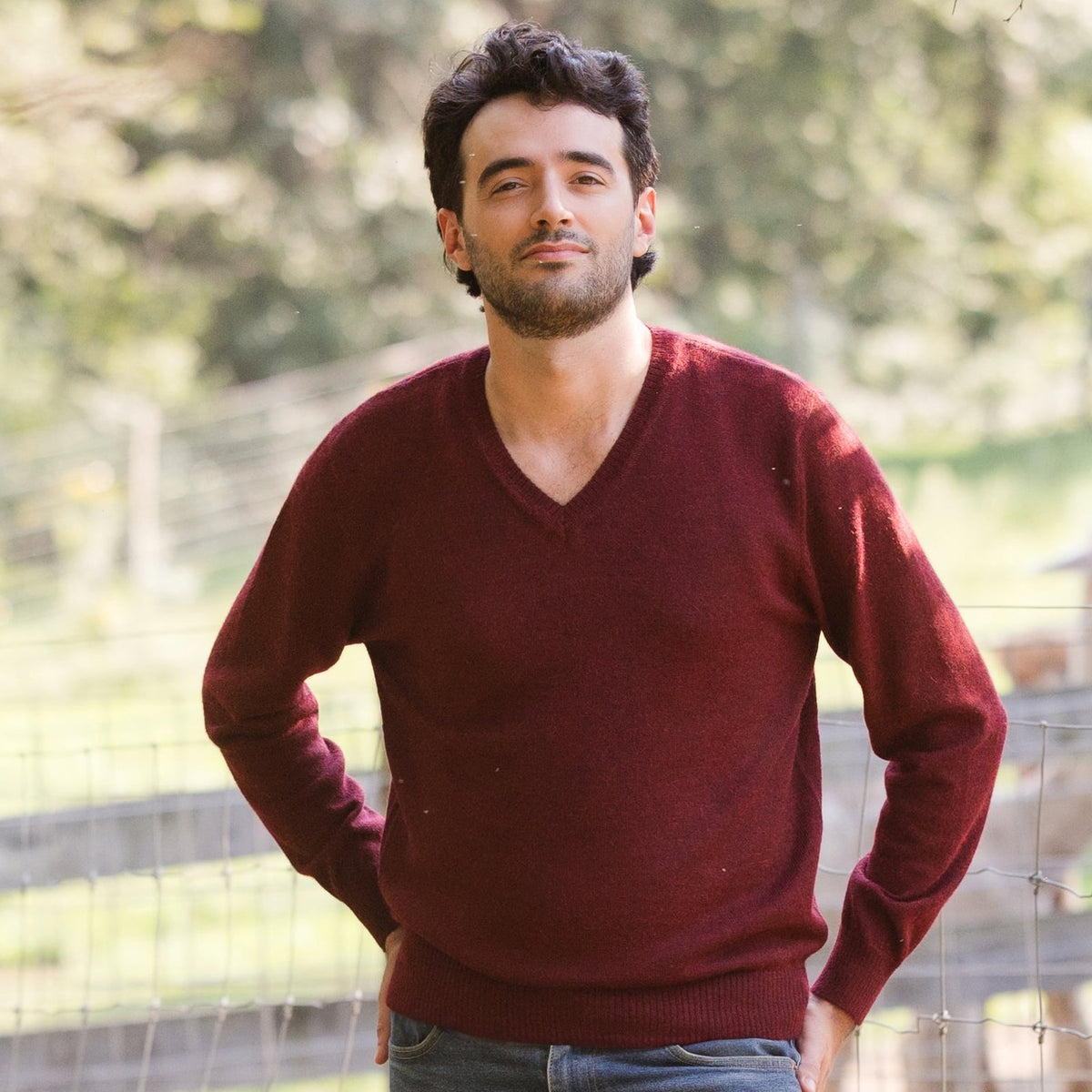 A man wearing a red v-neck baby alpaca sweater, standing outdoors.
