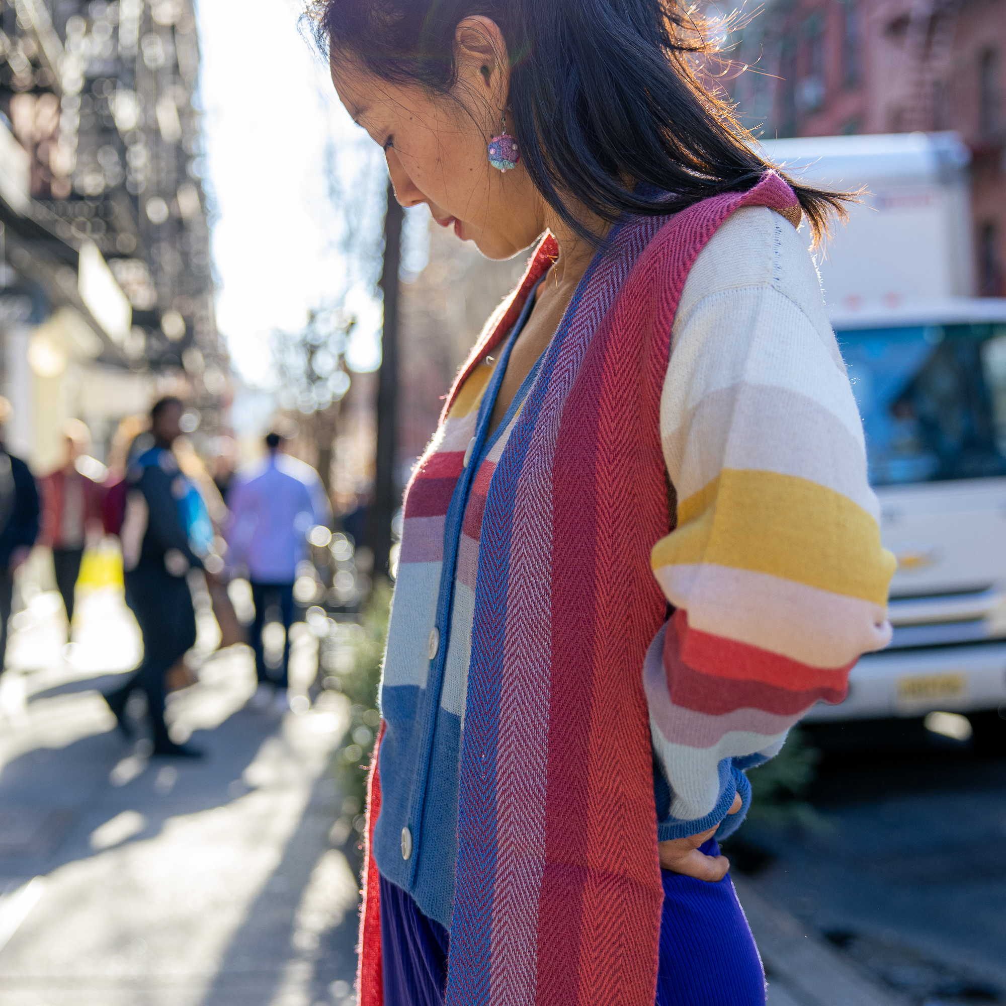 Woman wearing a colorful scarf and striped sweater on a city street.