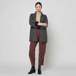 Woman wearing a patterned coat, beige sweater, brown pants, and black boots on a white background