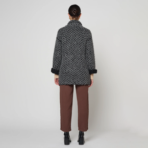 Person wearing a patterned coat and brown pants on a white background