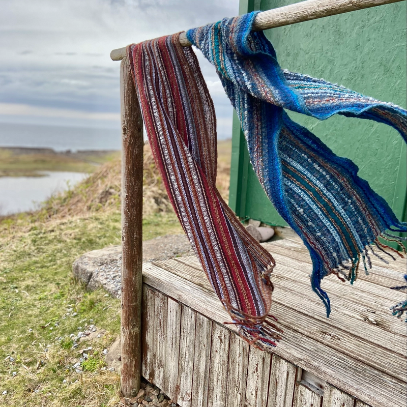 Striped scarves draped over a wooden railing with a scenic background