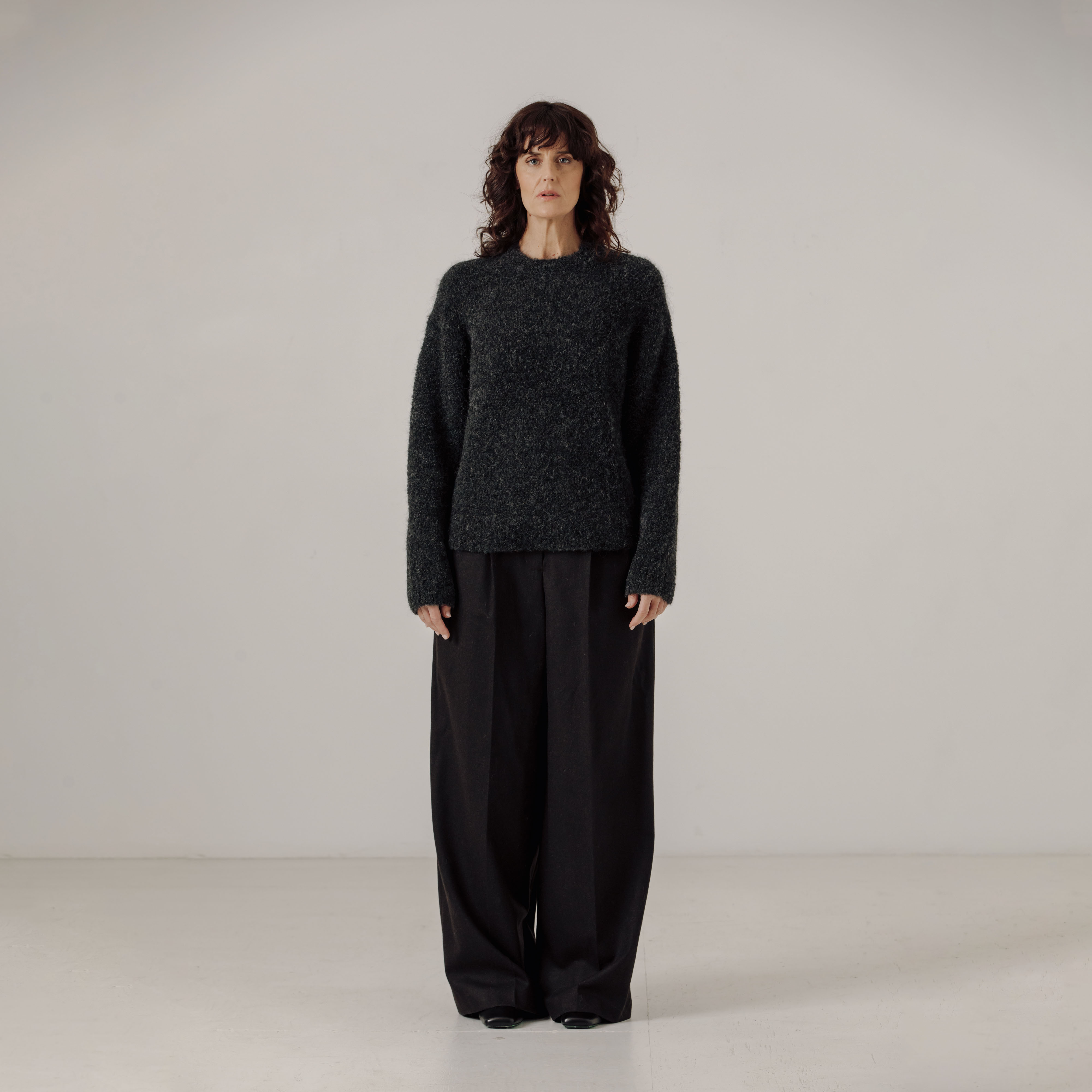 Person wearing a dark gray boucle sweater and black pants on a plain background