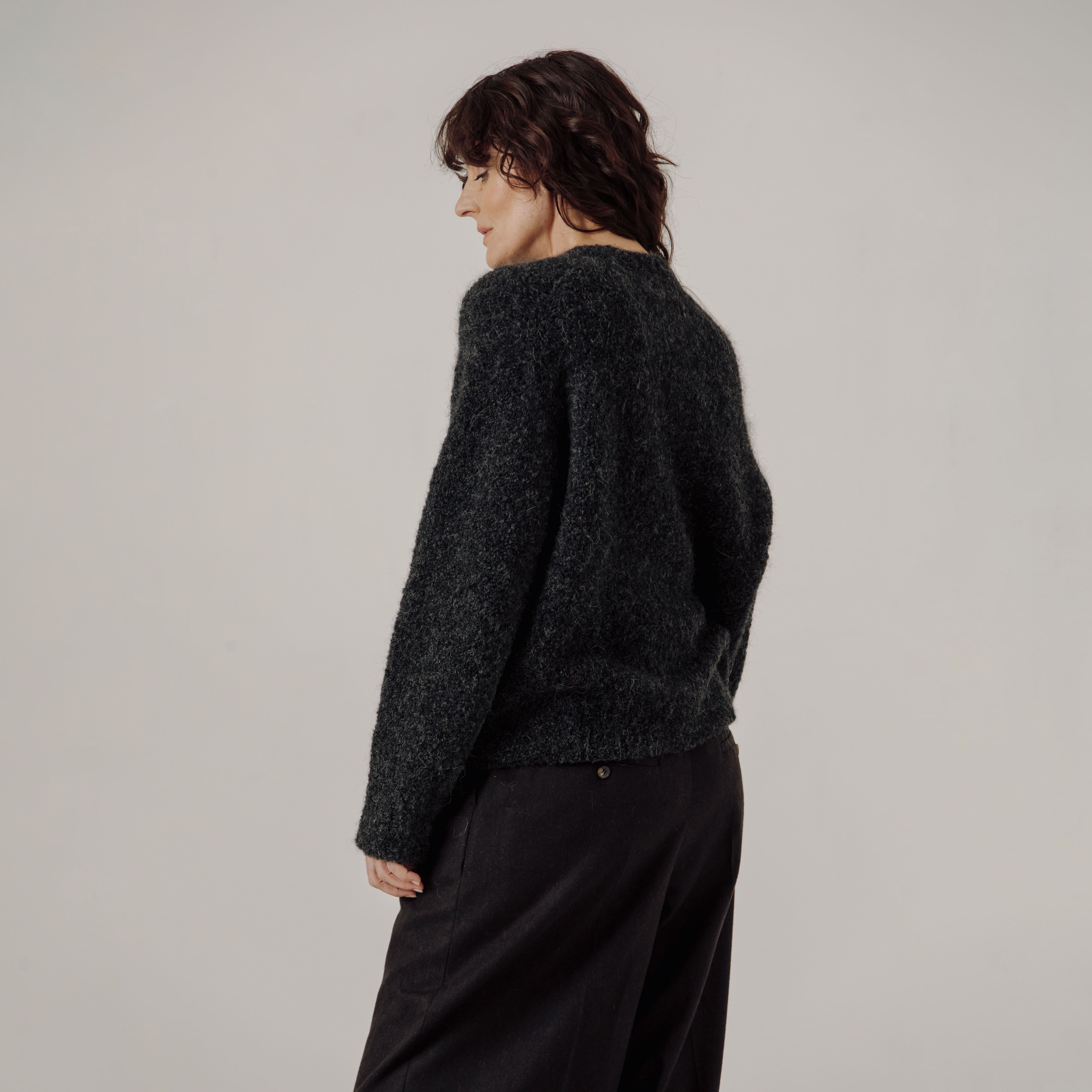 Person wearing a dark gray boucle sweater and black pants on a plain background