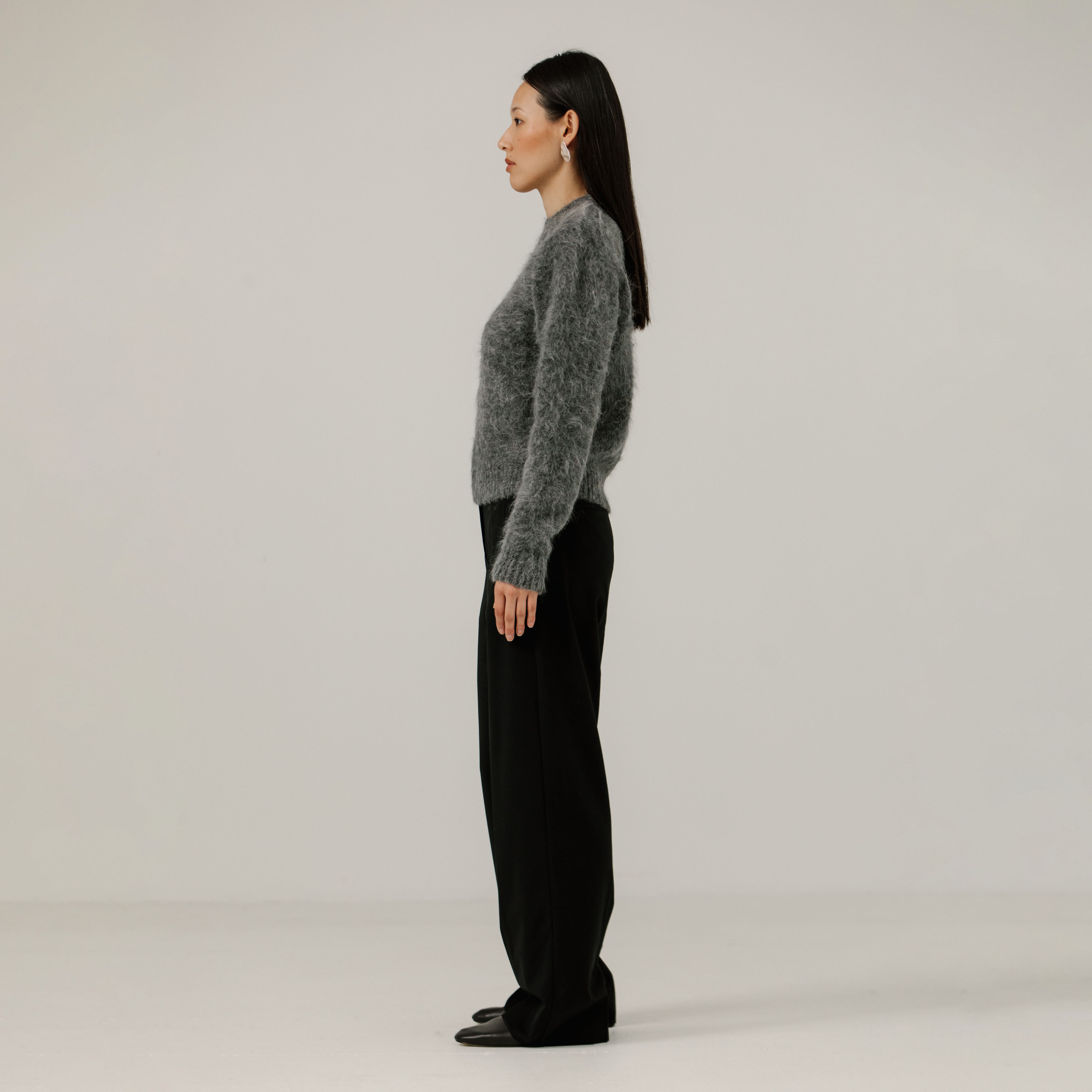Woman wearing a gray textured sweater and black pants on a plain background