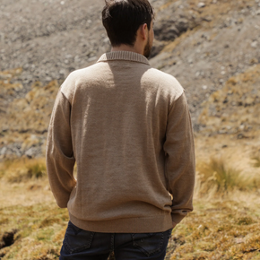 Man wearing a beige sweater standing in a mountainous landscape