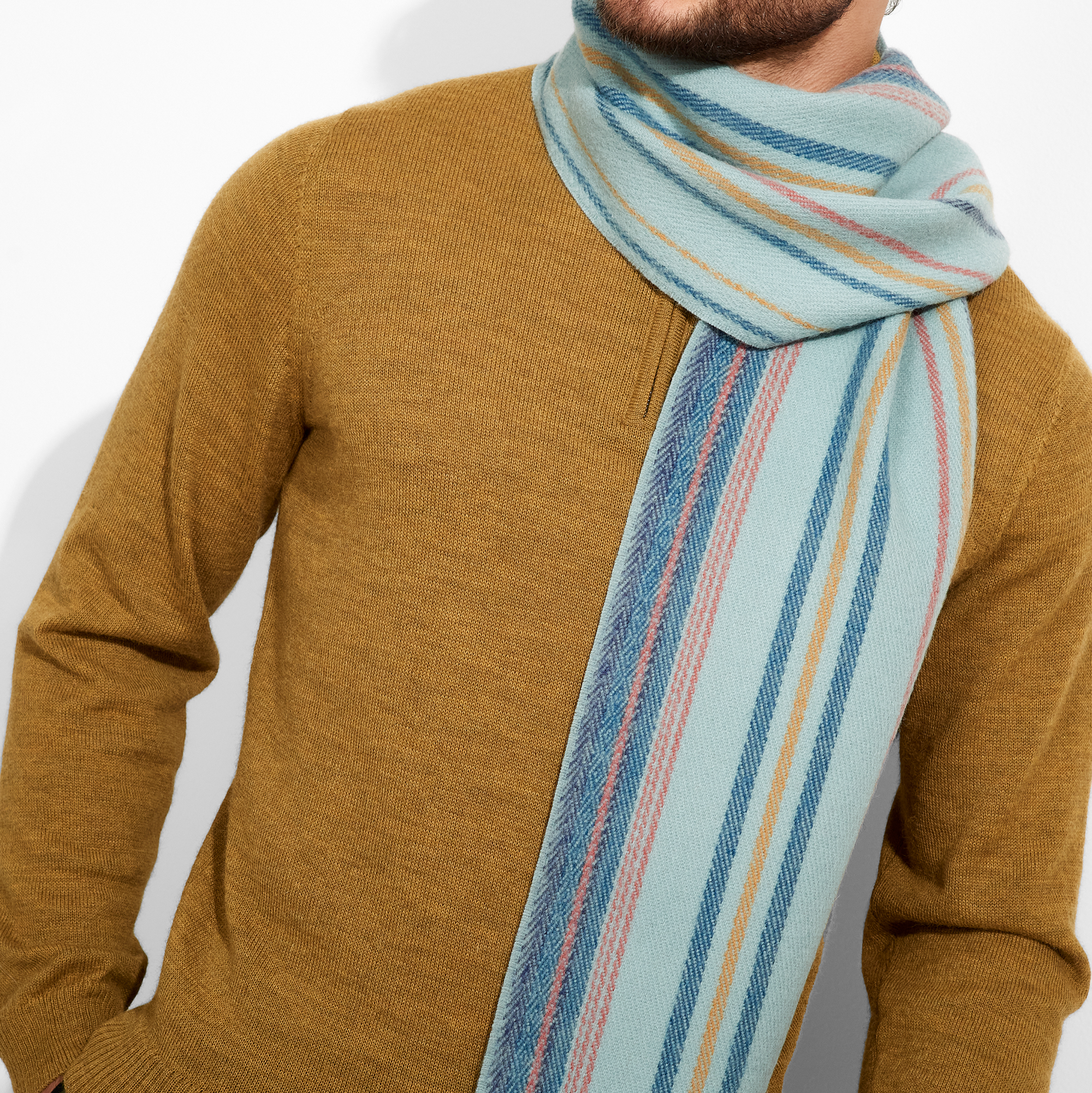 Man wearing a mustard sweater and a striped scarf with a neutral background