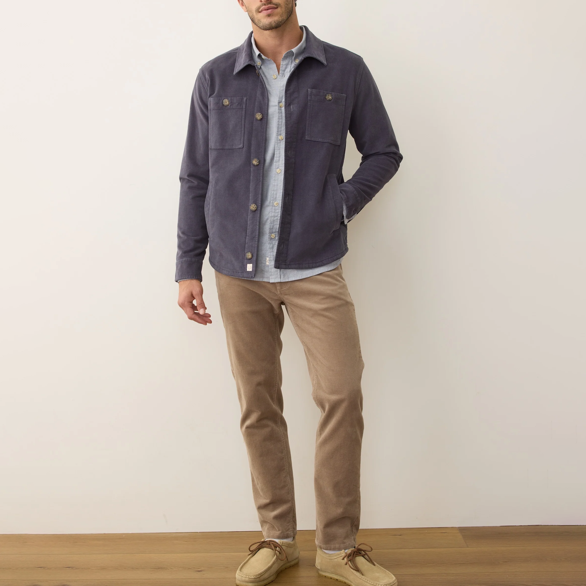 Man wearing a dark blue jacket over a light shirt with beige pants against a plain background