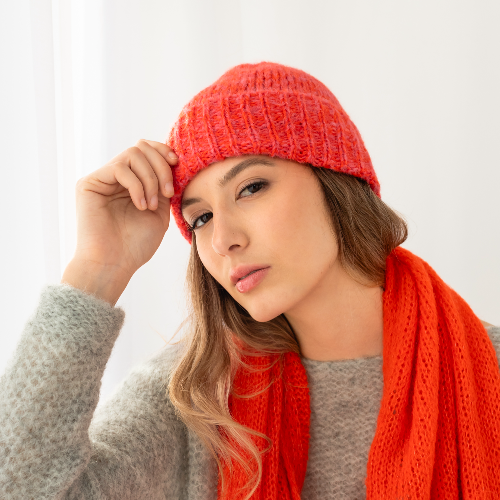 Woman wearing a red knitted hat and shawl against a white background