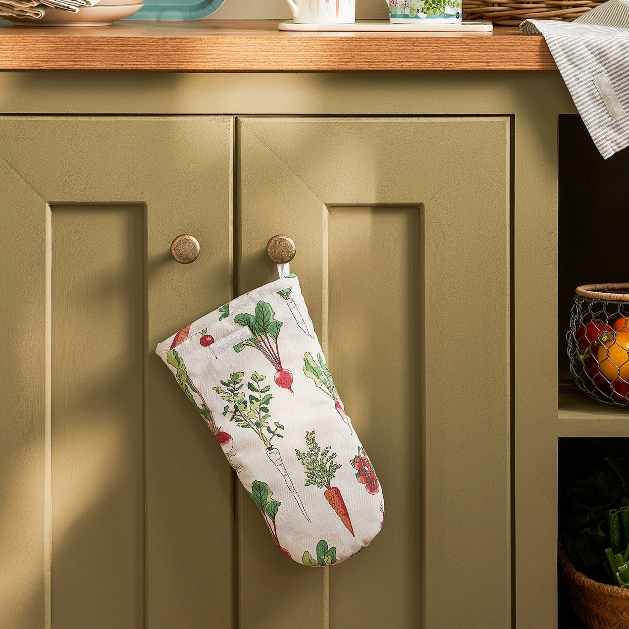 Oven mitt with vegetable pattern hanging on a green cabinet