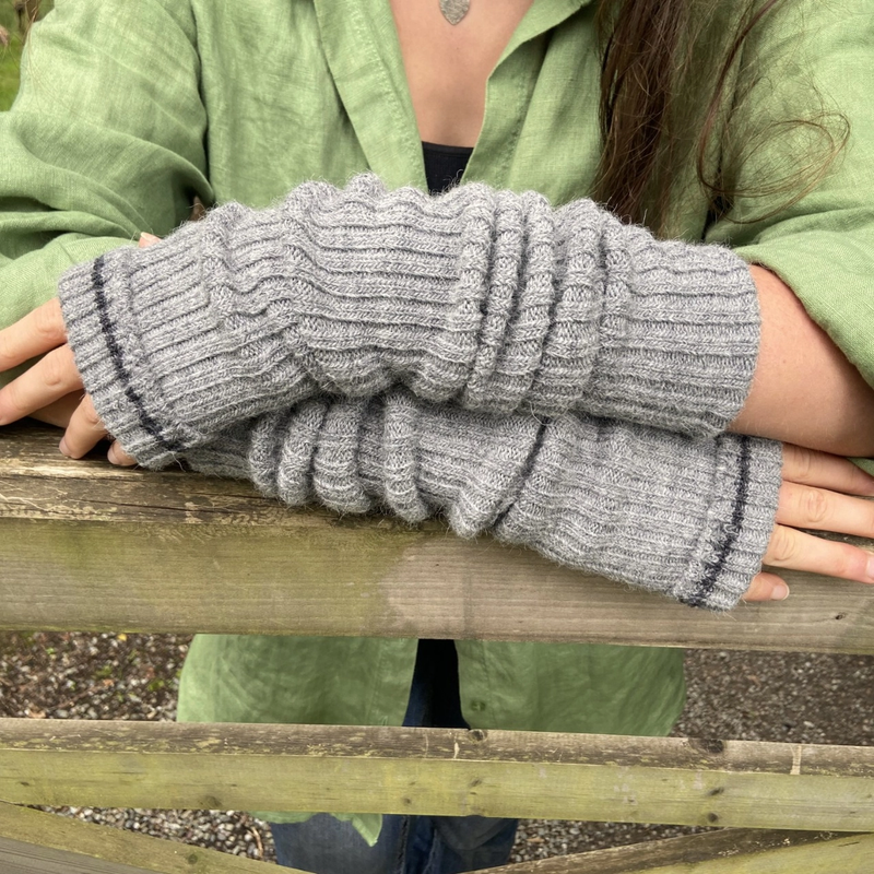 Person wearing gray ribbed arm warmers standing at a wooden fence.