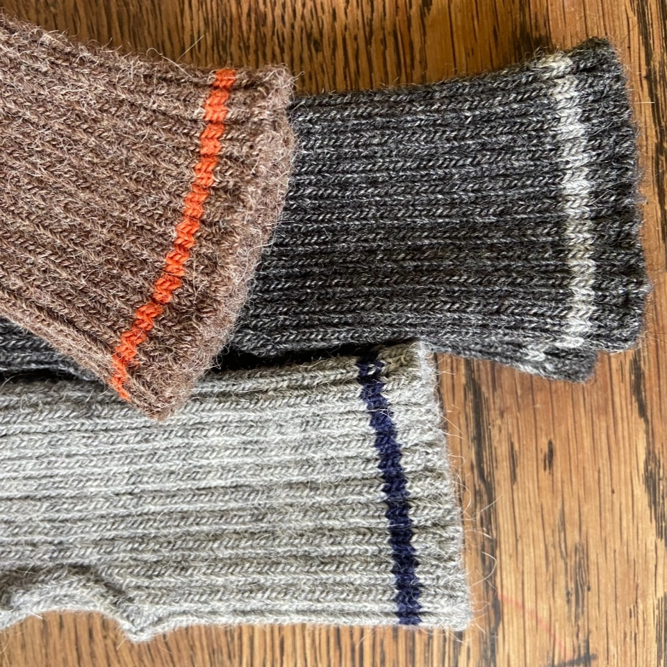 Three pairs of knitted wrist warmers in different colors on a wooden surface