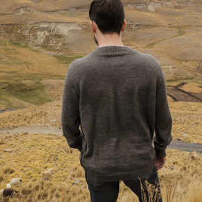 Man wearing a gray sweater standing in a field with mountains in the background