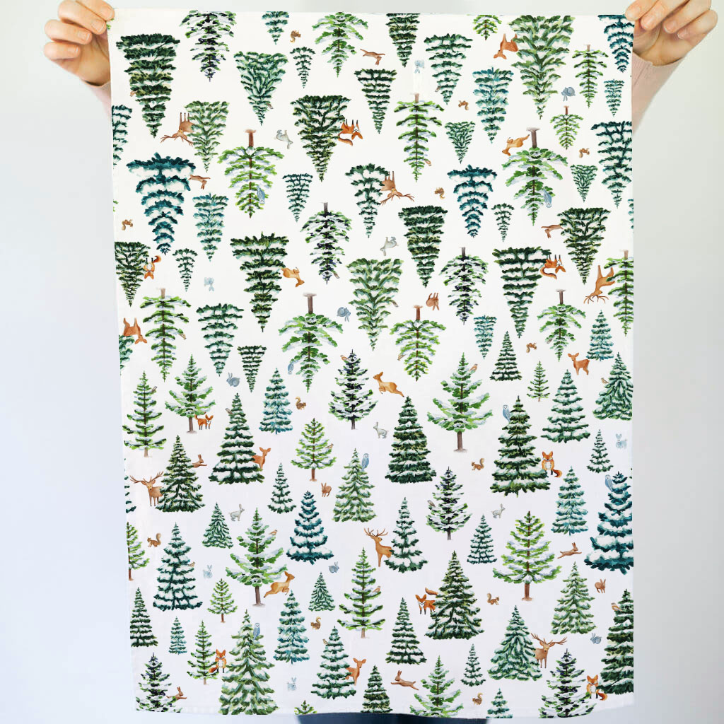 Patterned tea towel with trees and animals held by two hands against a light background