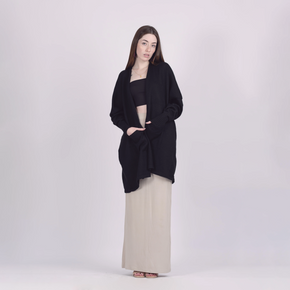 Woman wearing a black cardigan over a black top and beige pants on a white background