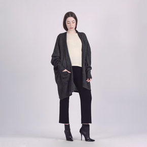 Woman wearing a dark gray cardigan over a white top and black pants on a light gray background