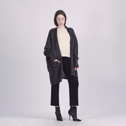 Woman wearing a dark gray cardigan over a white top and black pants on a light gray background