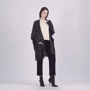 Woman wearing a long dark gray cardigan over a light sweater and black pants on a white background