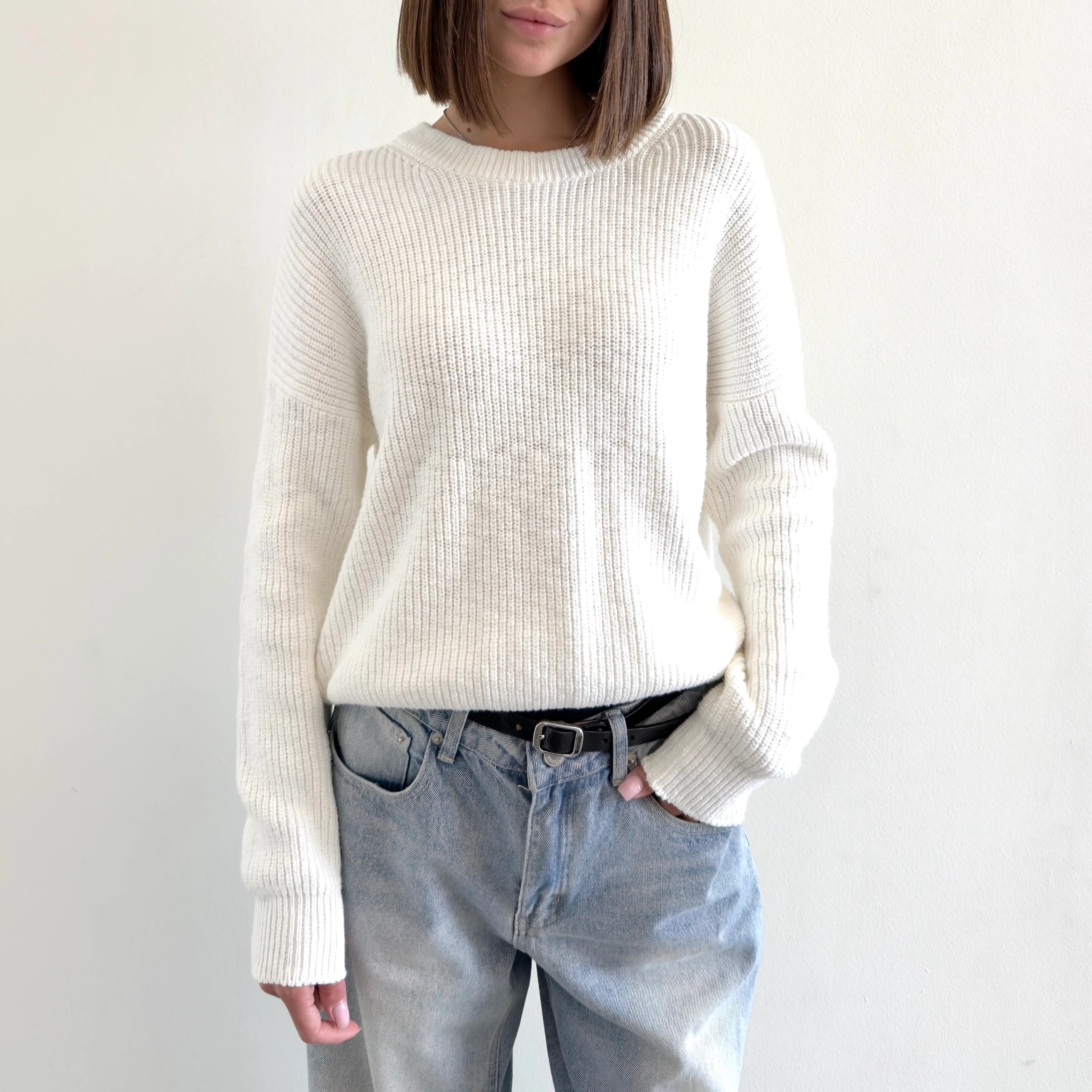 Person wearing a white sweater and light blue jeans against a plain background
