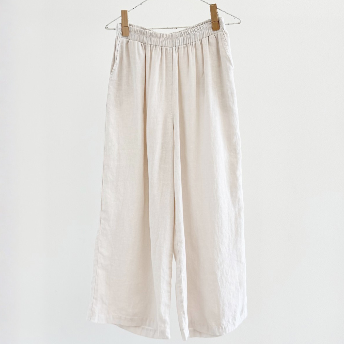 Beige pants hanging on a wooden hanger against a white background