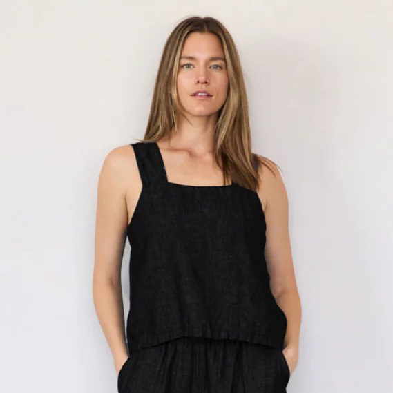 Woman wearing a black sleeveless top and black pants against a plain background