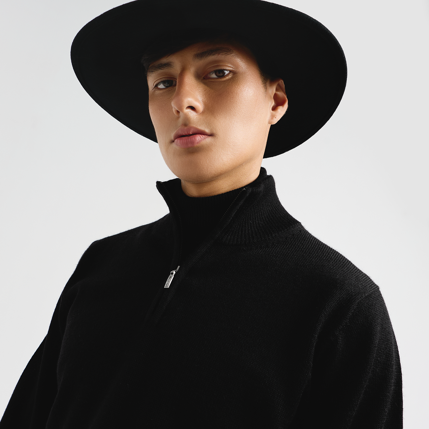 Person wearing a black hat and black sweater against a light gray background