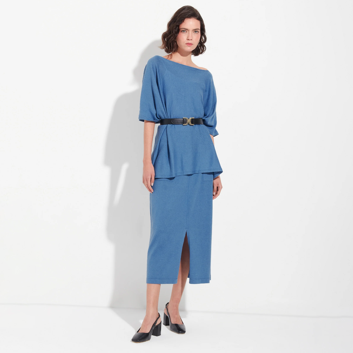 Woman wearing a blue poncho and skirt with a belt on a white background
