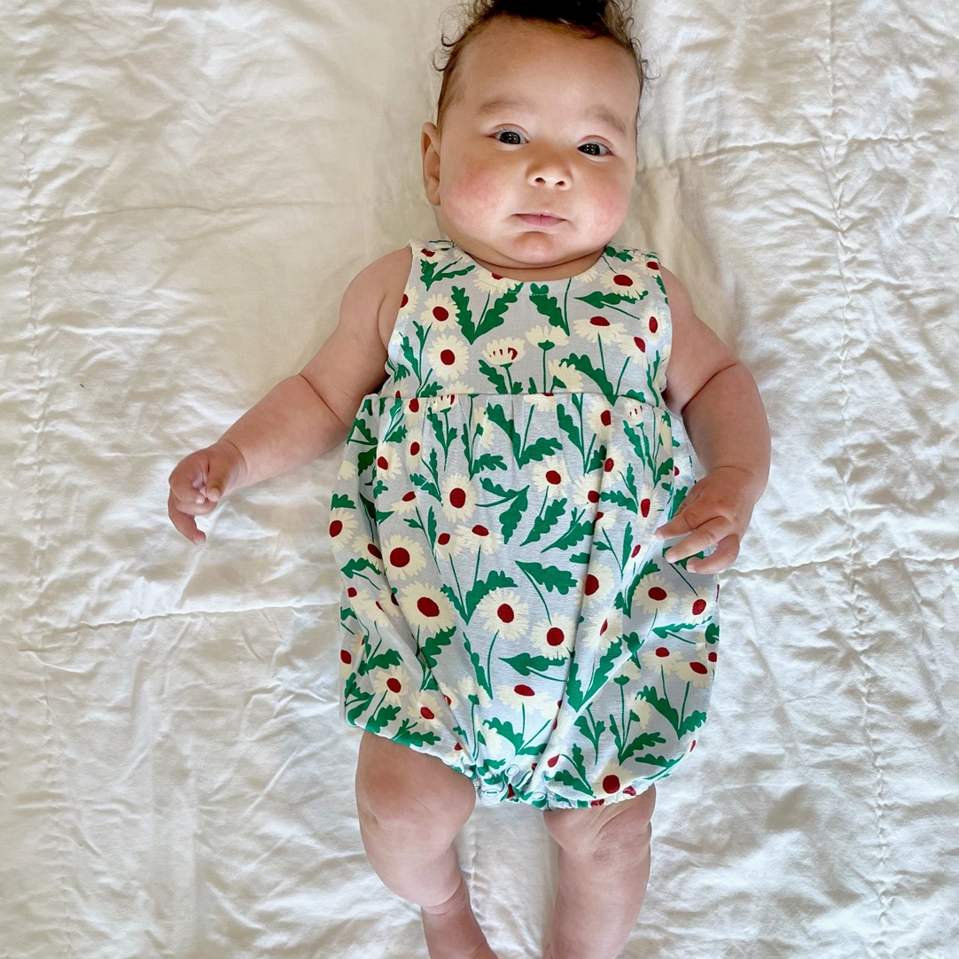 Baby wearing a floral romper lying on a white bed