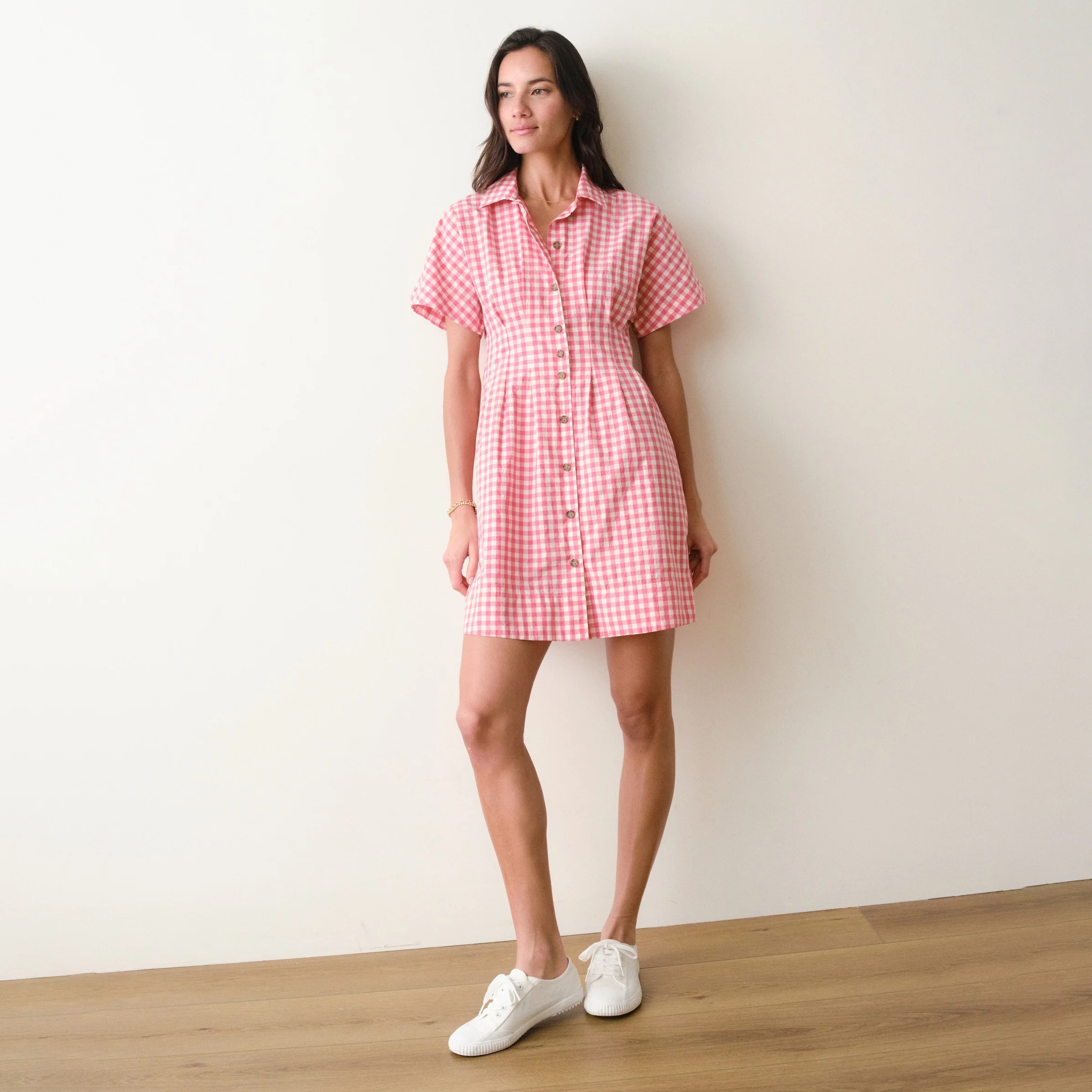 Woman wearing a red and white checkered dress standing against a plain wall.