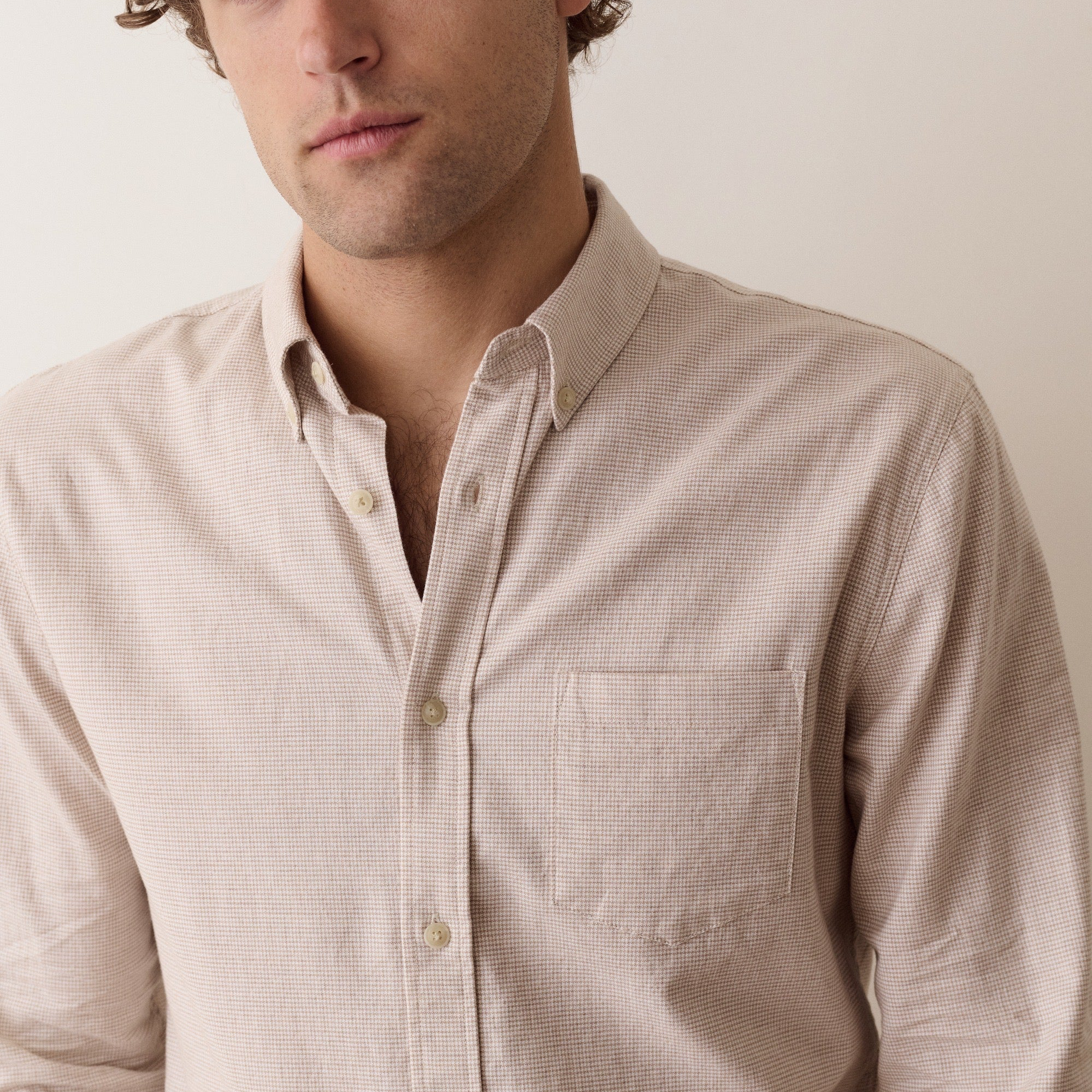 A close-up of a man wearing a light beige textured long-sleeve button-down shirt with a chest pocket, set against a plain off-white background.