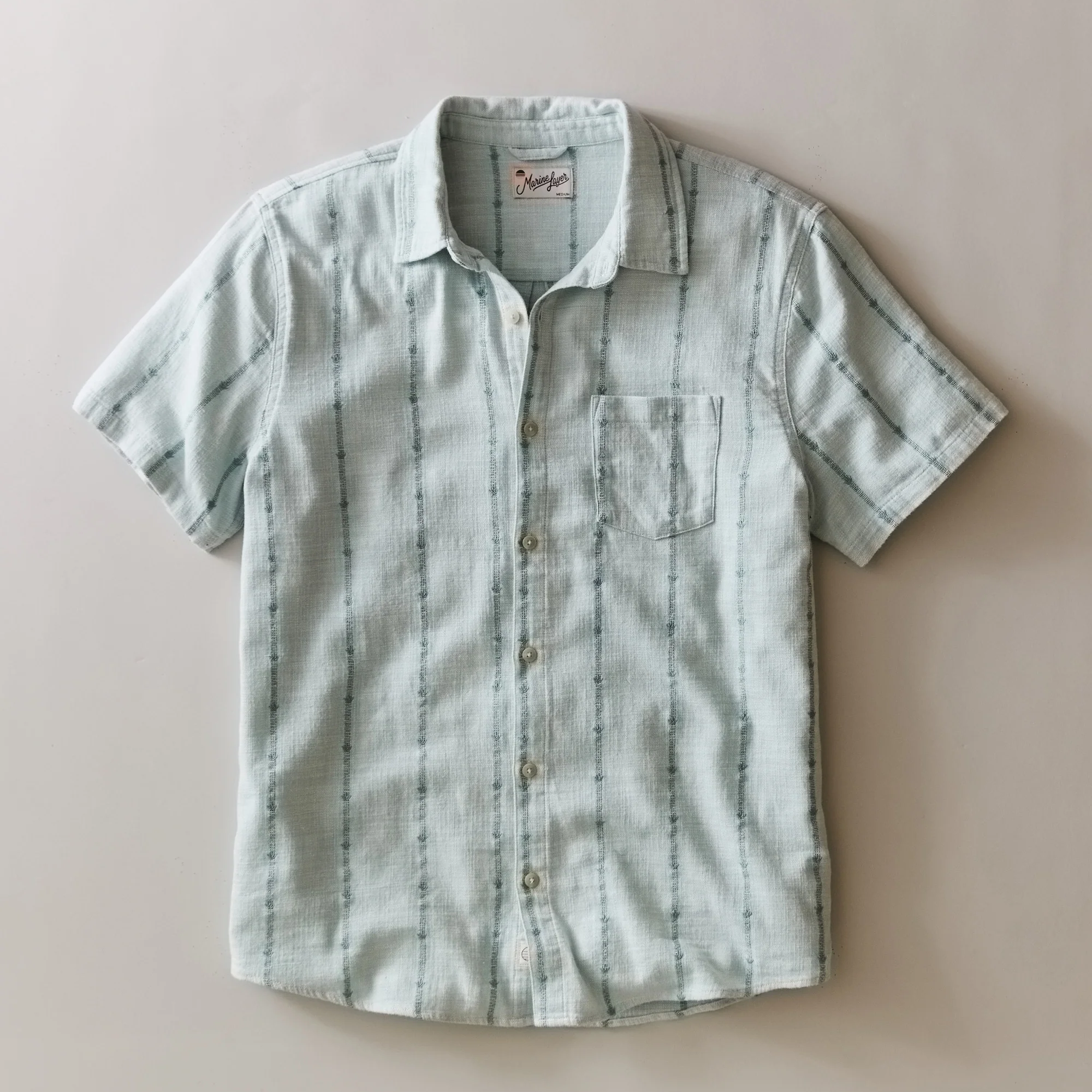 Short-sleeve button-up shirt with subtle pattern on a beige background