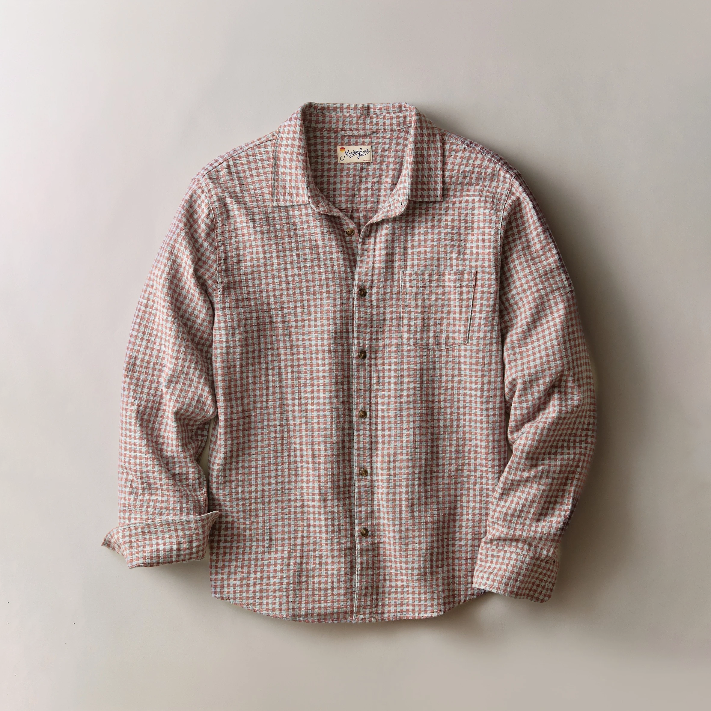 A long-sleeve button-up shirt with a fine red gingham check pattern, laid flat against a neutral light gray background.