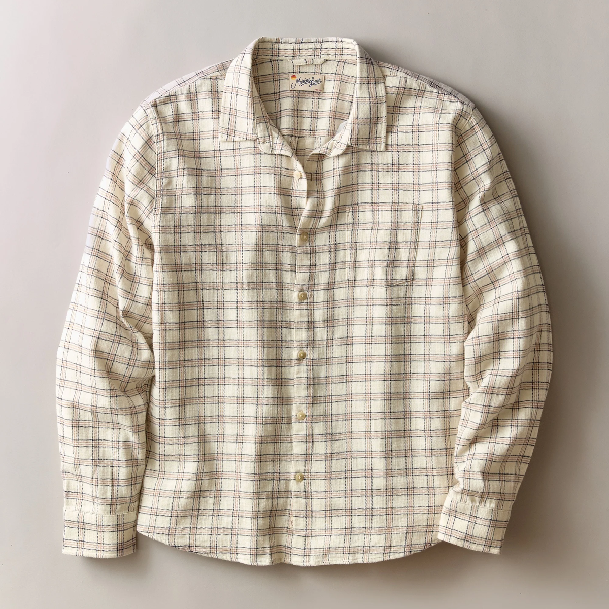 A long-sleeve button-up shirt in a cream and beige plaid pattern with thin brown and blue lines, laid flat against a neutral gray background.