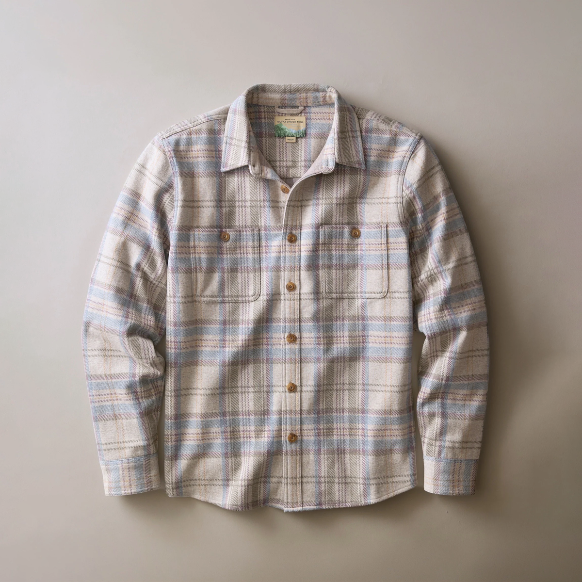 A long-sleeve button-up shirt with a plaid pattern in beige, light blue, and brown, laid flat against a neutral gray background.