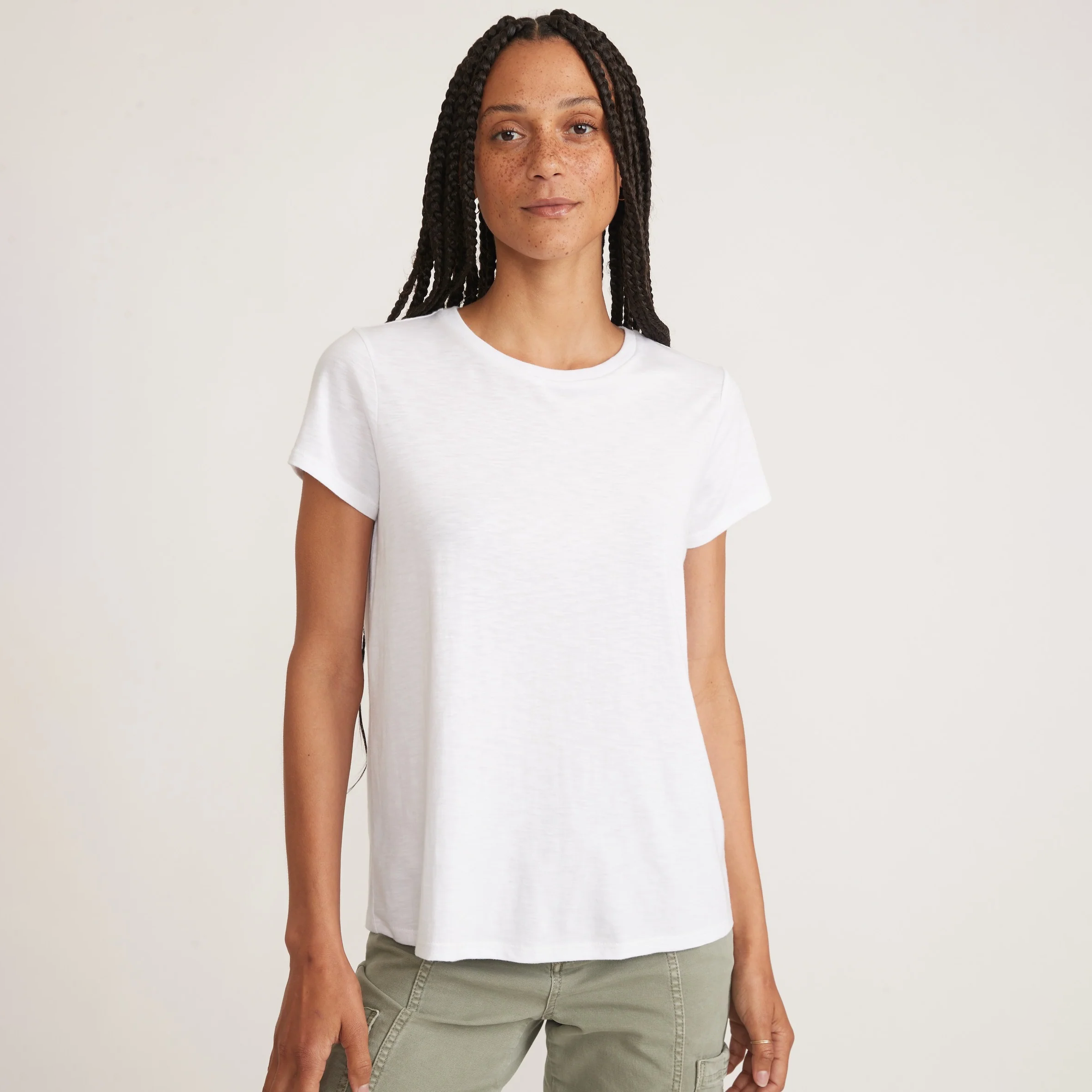 Woman wearing a white tee and green pants on a neutral background.