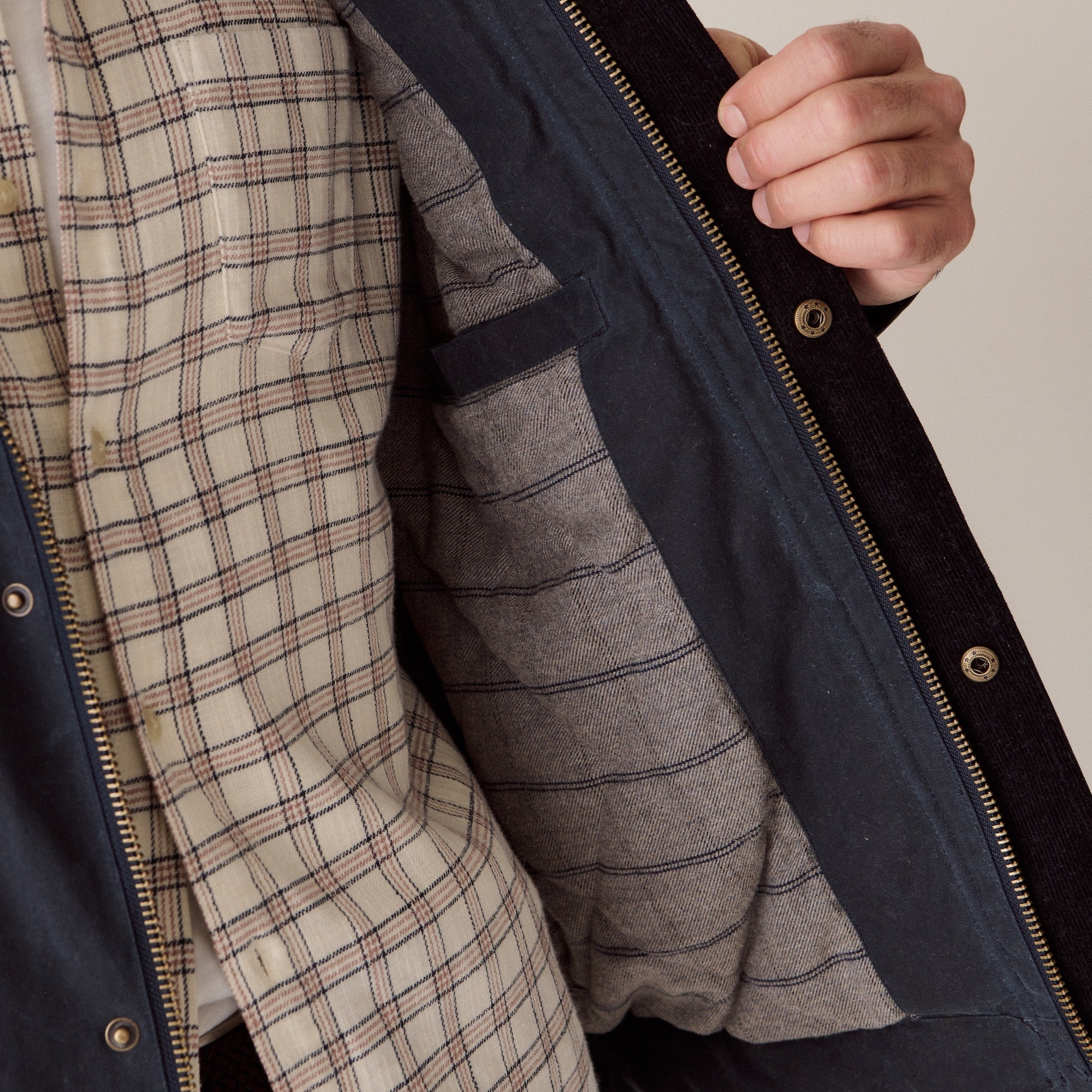 Close-up of a person wearing a navy jacket with a grey striped lining and a beige plaid shirt, holding the jacket open to show the interior details.