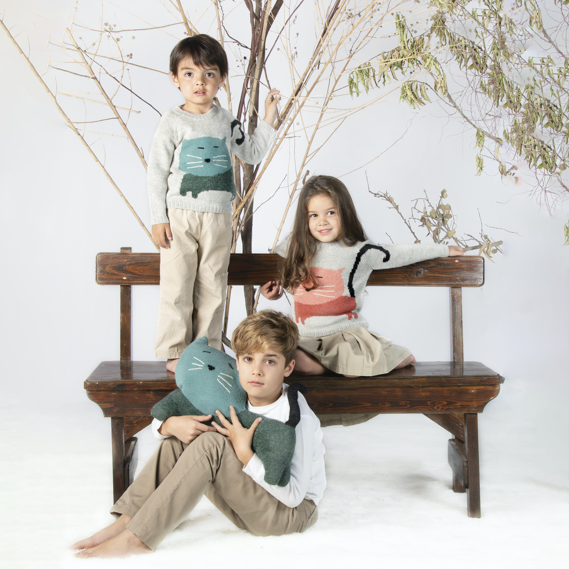 Three children sitting on a wooden bench with decorative branches in the background